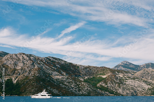 The white luxury yacht sails on the Bay of Kotor in Montenegro  against the background of mountains  blue sky with clouds.