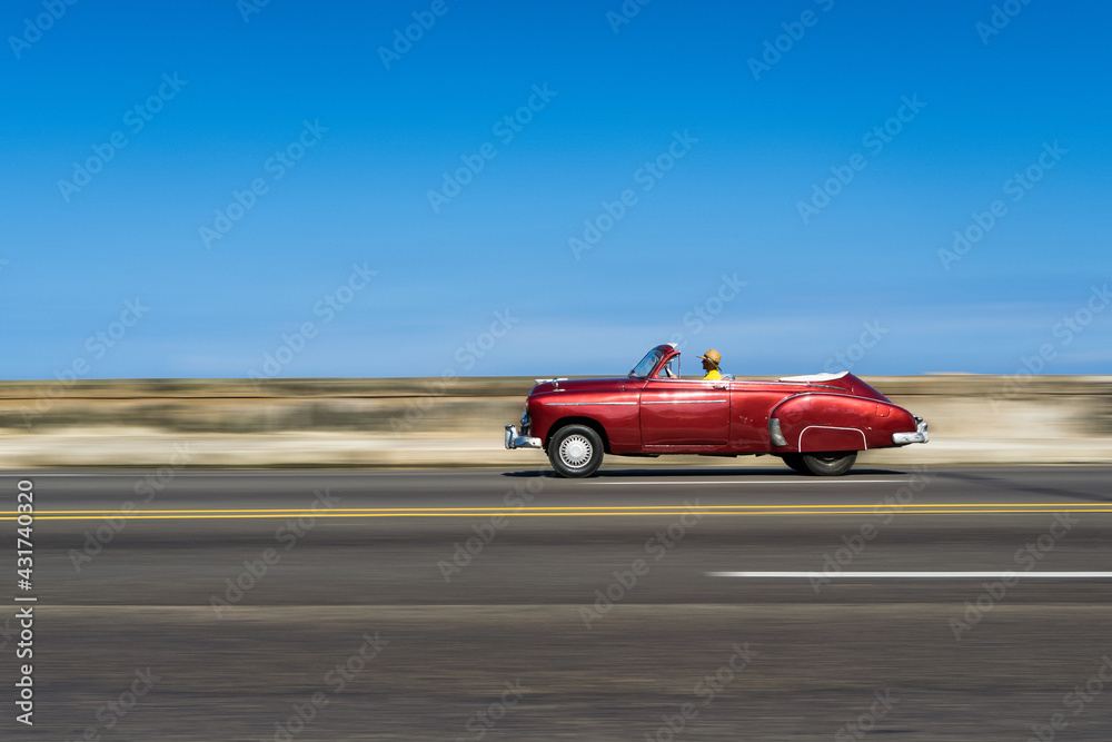 A red classic car driving along the Malecon in Havana, Cuba.