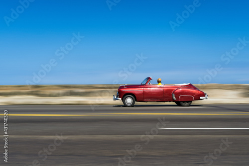 A red classic car driving along the Malecon in Havana, Cuba.