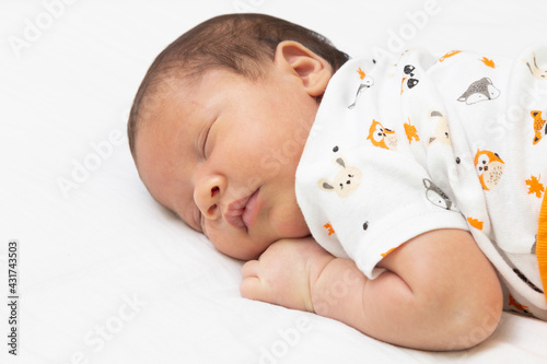 baby sleeping in bed with his arms under his head.