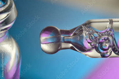 Cosmetic pipette with drops of transparent liquid and a jar, close-up on a colored background.