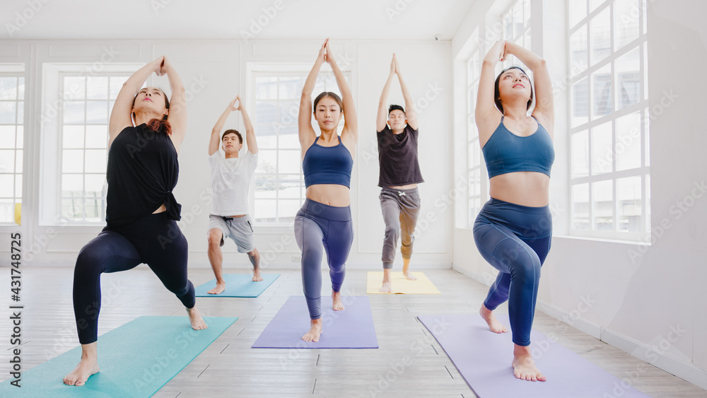 Fototapeta premium Young Asian sporty attractive people practicing yoga lesson with instructor. Asia group of women exercising healthy lifestyle in fitness studio. Sport activity, gymnastics or ballet dancing class.
