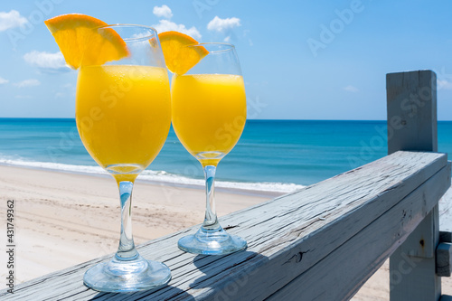 Two glasses with mimosa cocktail. Yellow drink with bubbles glows in the sun on the background of the beach by the ocean in calm weather