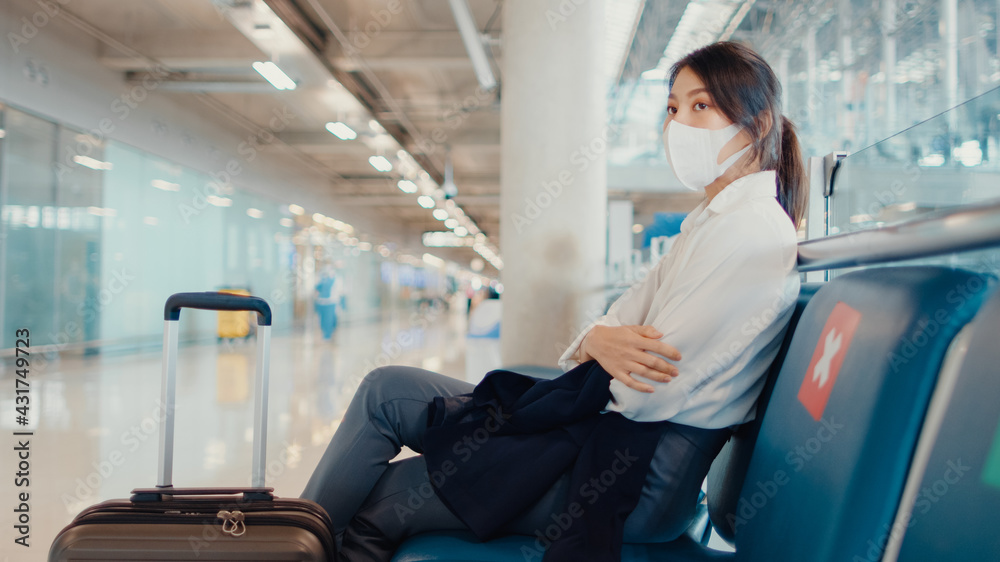 Asian business girl walk with luggage sitting in bench wait and look partner for flight at airport. Business travel commuter covid pandemic, Business travel social distancing, Business travel concept. Asian business girl walk with luggage sitting in bench wait and look partner for flight at airport. Business travel commuter covid pandemic, Business travel social distancing, Business travel concept.