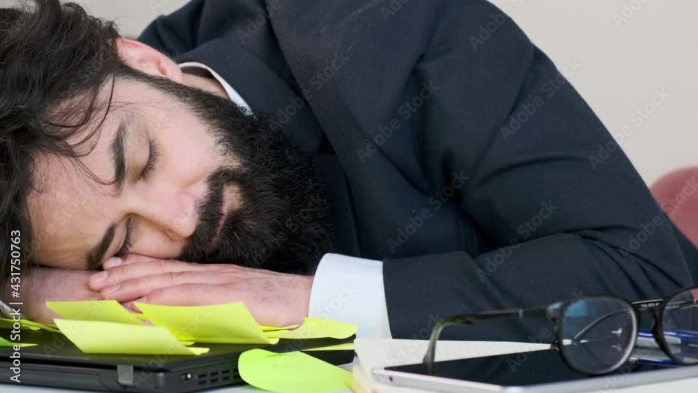 Close up of an exhausted and tired businessman sleep with his head on computer. Many reminder notes on the table, multitasking concept. Close up of an exhausted and tired businessman sleep with his head on computer. Many reminder notes on the table, multitasking concept.