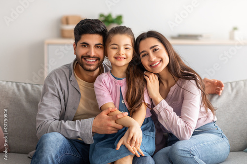 Family portrait. Excited arabic parents and cute little daughter posing together, embracing and smiling to camera