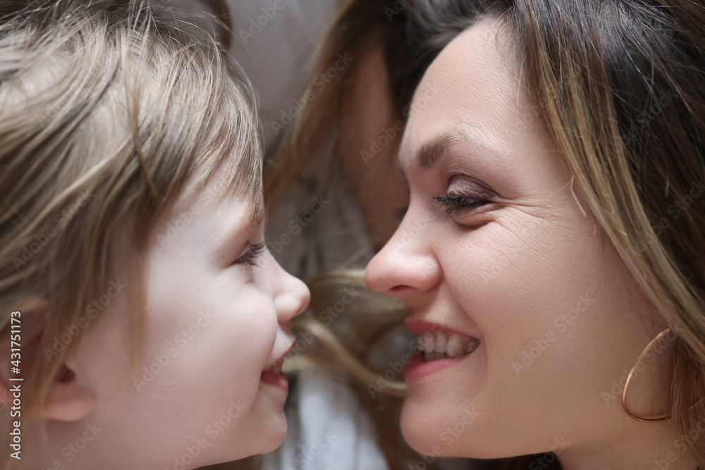 Happy mom and daughter lie on pillow and look at each other