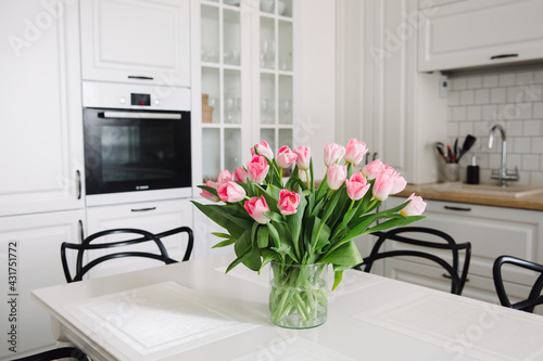 Bouquet of pink tulips in a transparent vase, on kitchen table. Flowers in interior.