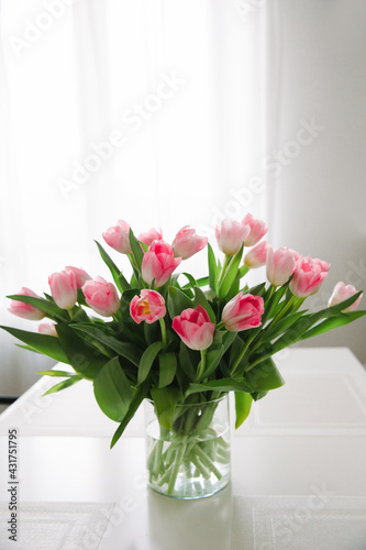 Bouquet of pink tulips in a transparent vase, on kitchen table. Flowers in interior.