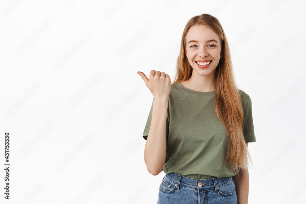 Your logo here. Smiling confident girl student pointing thumb left and looking determined, give advice, recommend this product, showing advertisement on copy space, white background Your logo here. Smiling confident girl student pointing thumb left and looking determined, give advice, recommend this product, showing advertisement on copy space, white background