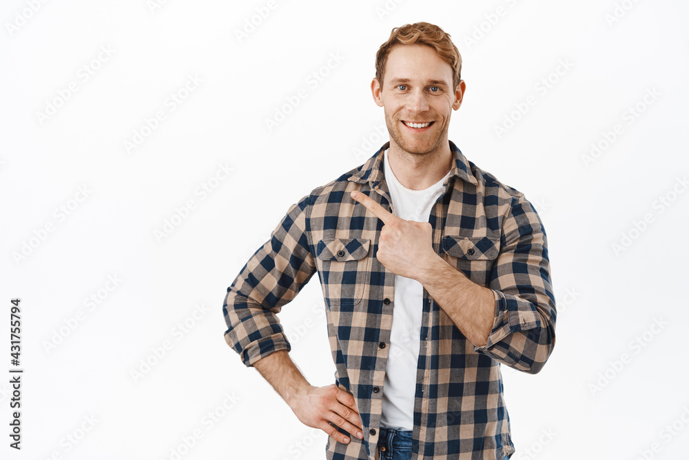 Confident attractive man with red hair and beard, pointing finger at upper left corner, showing new promo deal, shop offer, demonstrating promotional text, standing over white background