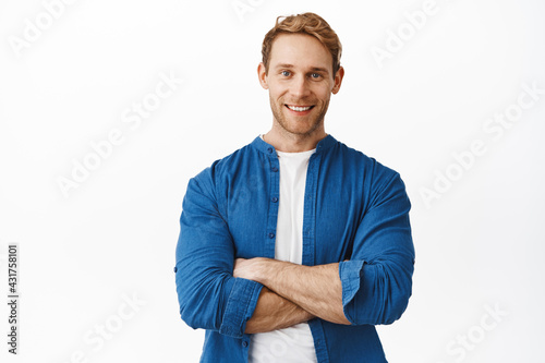 Confident handsome redhead man with arms crossed over body, smiling and looking determined like professional, standing in casual clothes against white background photo