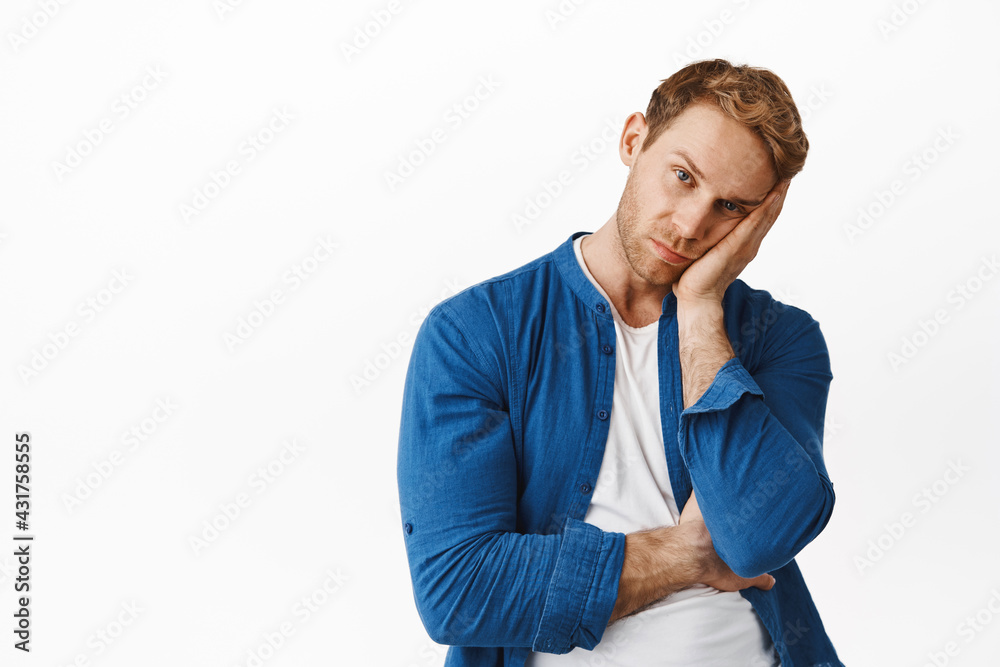 Portrait of bored redhead man lean exhausted face on hand, looking annoyed at something boring or uninteresting, standing reluctant against white background Portrait of bored redhead man lean exhausted face on hand, looking annoyed at something boring or uninteresting, standing reluctant against white background