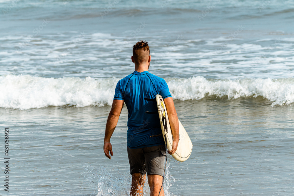 Naklejka premium Surfer z deską surfingową na tle oceanu, mężczyzna uprawiający zdrowe sporty wodne.