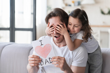 Little small daughter kid making surprise present for her father for father`s day, giving him a postcard with heart. I love you, dad! Family holiday, spending time together, congratulations
