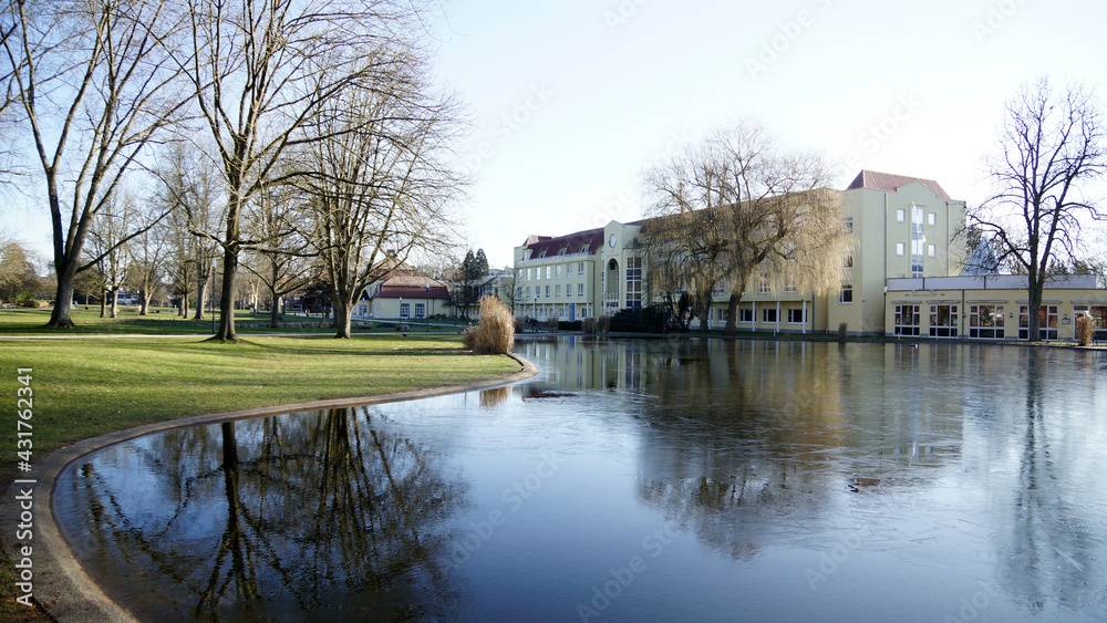 Jugendstil Kurhaus vor Seenfläche und kahlen Bäumen im Kurpark in Bad Hersfeld im Frühling mit Sonne ohne Menschen