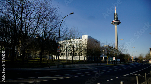 Der Europaturm / frankfurter Spargel, Fernmeldeturm in Frankfurt am Main zwischen Baumen und Wohnhäusern vor blauem Himmel