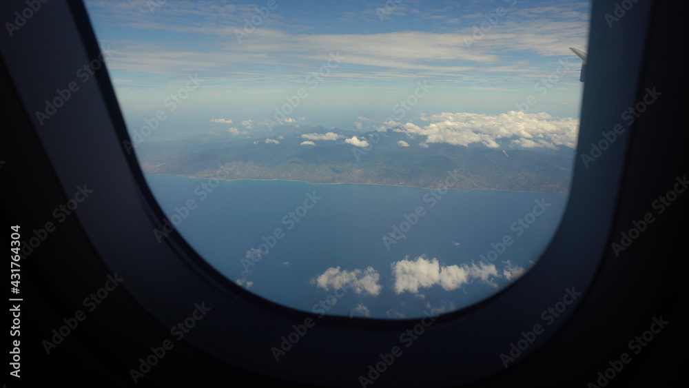 Airplane flying over blue sea and tropical island. Airplane wing through the porthole. Looking through window aircraft during flight