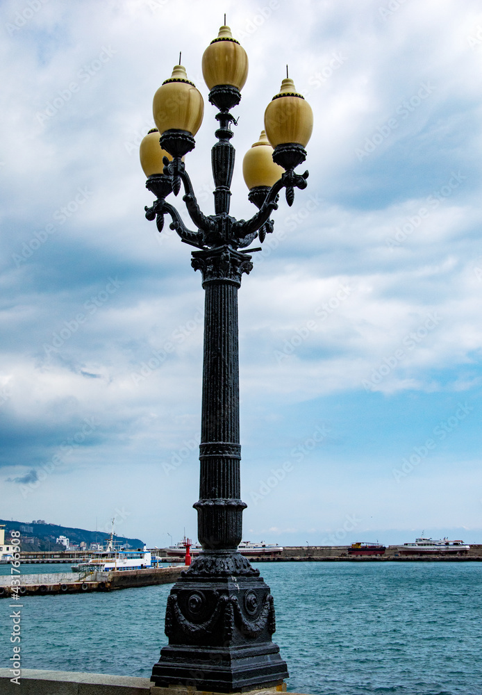 A beautiful lamppost with five bulbs stands on the embankment. A lamppost is captured against the background of the blue sky and sea