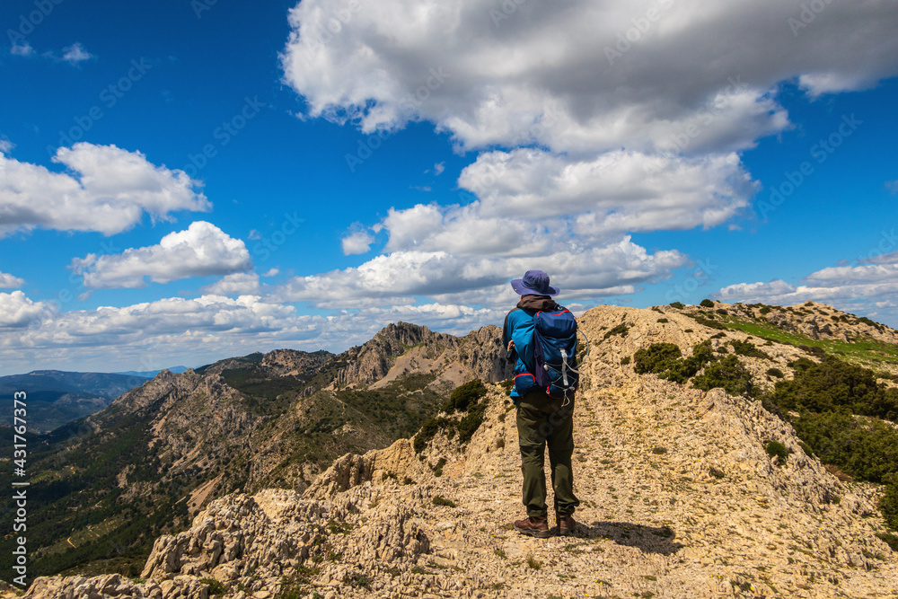 Lonely hiker, walking up a mountain, on a sunny and cloudy day, through the Alicante mountain of La Mallada del Llop.