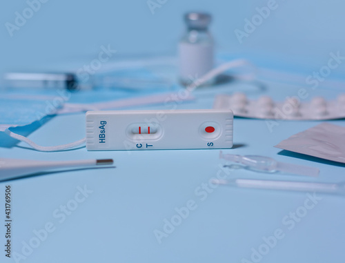 Rapid test cassette for Hepatitis B Virus Test (HBsAg),medical mask, syringe,thermometer,medicine on a blue background.Test shows a positive result.Copy space photo