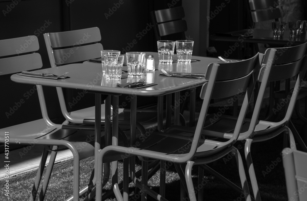 Empty cafe terrace setting for lunch. Nobody. Abandoned lifestyle background. Impossible dinner party, socializing limits metaphor, economic crisis concepts. Black white toned photo.