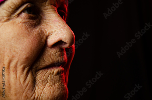 Old grandmother's face close up. Close-up of wrinkled old face. A portrait photo of an old grandmother. An old face in the dark. Aged skin on the face. Seniors concept