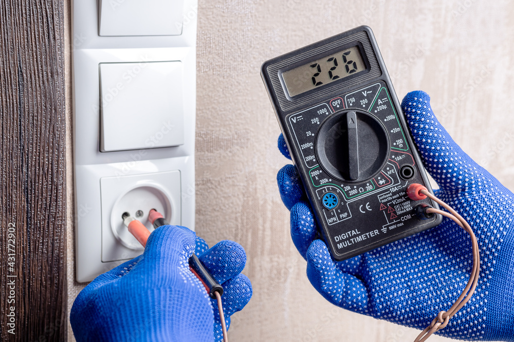 handyman electrician measuring wall outlet voltage at living room