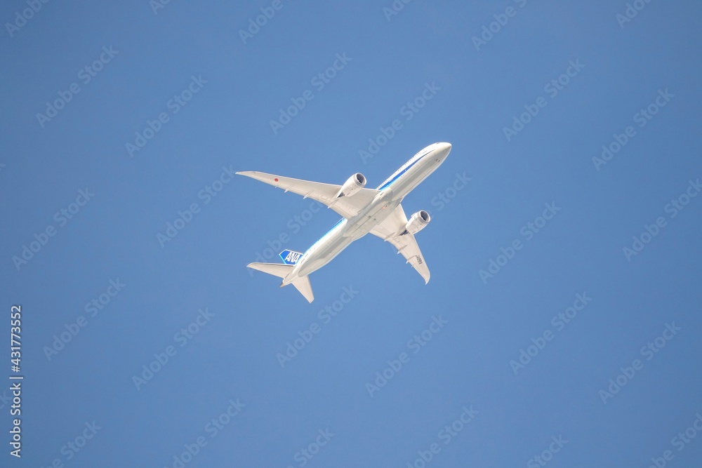 A close portrait of a touristic airliner plane flying low through a blue cloudless sky. It is a white airplane with a blue stripe on it. A close portrait of a touristic airliner plane flying low through a blue cloudless sky. It is a white airplane with a blue stripe on it.