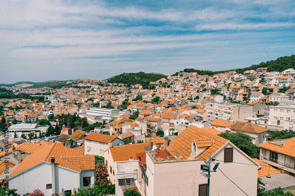 Orange roofs of old houses in Sibenik against a background of blue sky and greenery