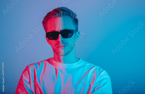 Portrait of fashion young man in white t-shirt and black sunglasses in red and blue neon light. © nikkimeel