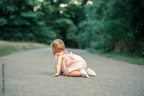  Cute baby girl crawling on road in park outdoor. Adorable child toddler exploring studying the world around. Healthy physical development. View from back behind. Authentic lifestyle happy childhood. photo