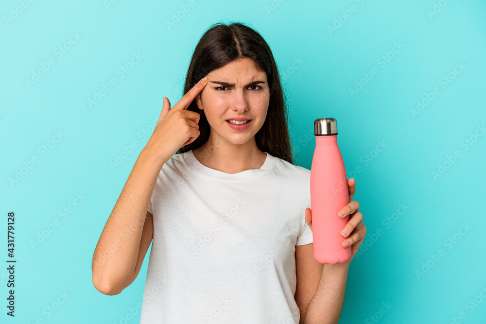 Young caucasian woman holding water bottle isolated on blue background showing a disappointment gesture with forefinger. Young caucasian woman holding water bottle isolated on blue background showing a disappointment gesture with forefinger.