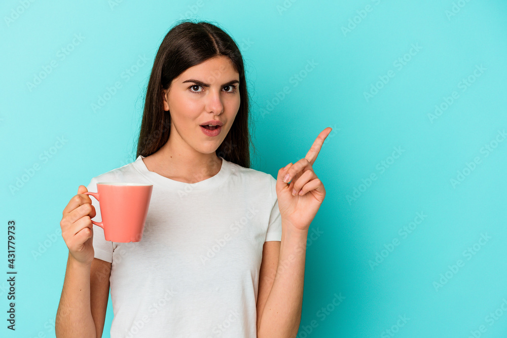 Young caucasian woman holding a mug isolated on blue background pointing to the side Young caucasian woman holding a mug isolated on blue background pointing to the side
