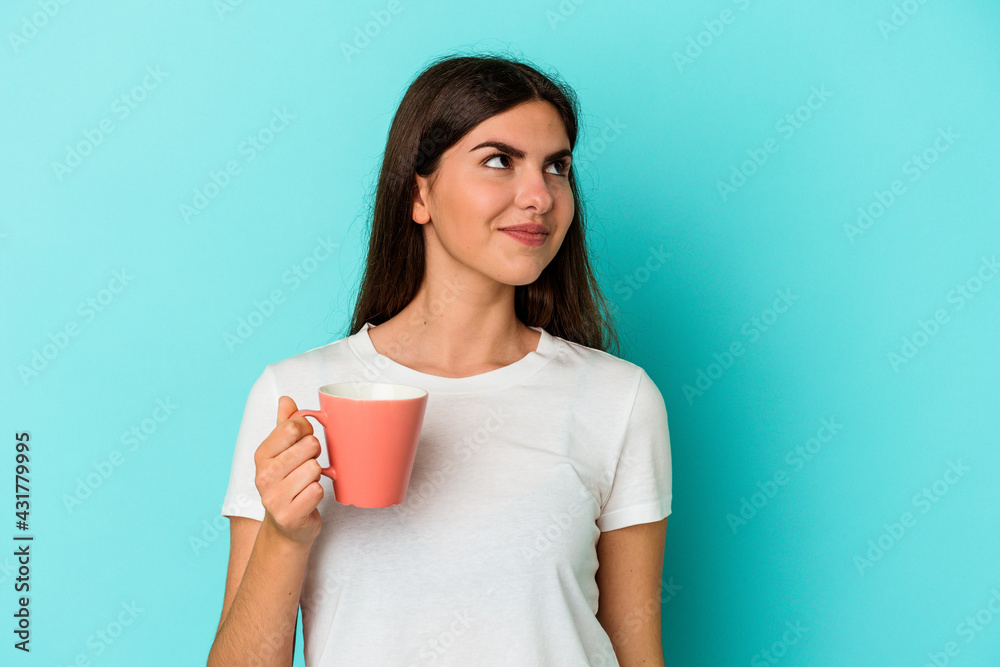 Young caucasian woman holding a mug isolated on blue background dreaming of achieving goals and purposes Young caucasian woman holding a mug isolated on blue background dreaming of achieving goals and purposes