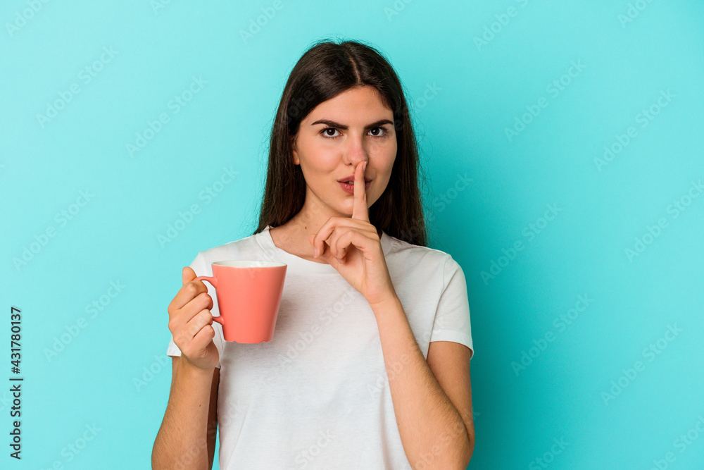 Young caucasian woman holding a mug isolated on blue background keeping a secret or asking for silence. Young caucasian woman holding a mug isolated on blue background keeping a secret or asking for silence.