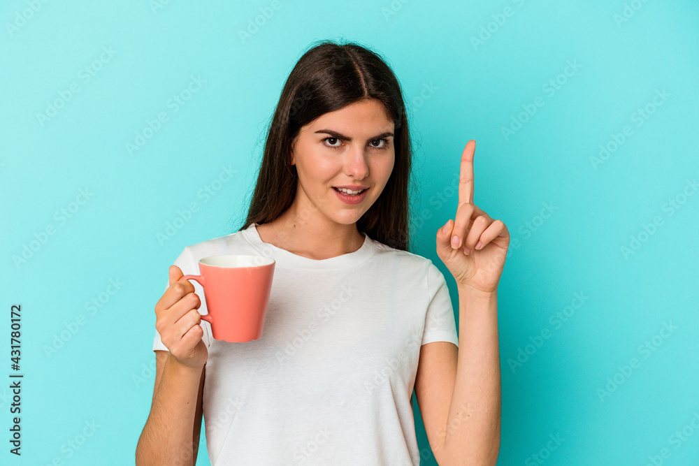 Young caucasian woman holding a mug isolated on blue background having an idea, inspiration concept. Young caucasian woman holding a mug isolated on blue background having an idea, inspiration concept.