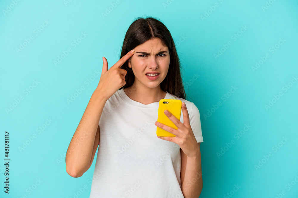 Young caucasian woman holding a mobile phone isolated on blue background showing a disappointment gesture with forefinger. Young caucasian woman holding a mobile phone isolated on blue background showing a disappointment gesture with forefinger.