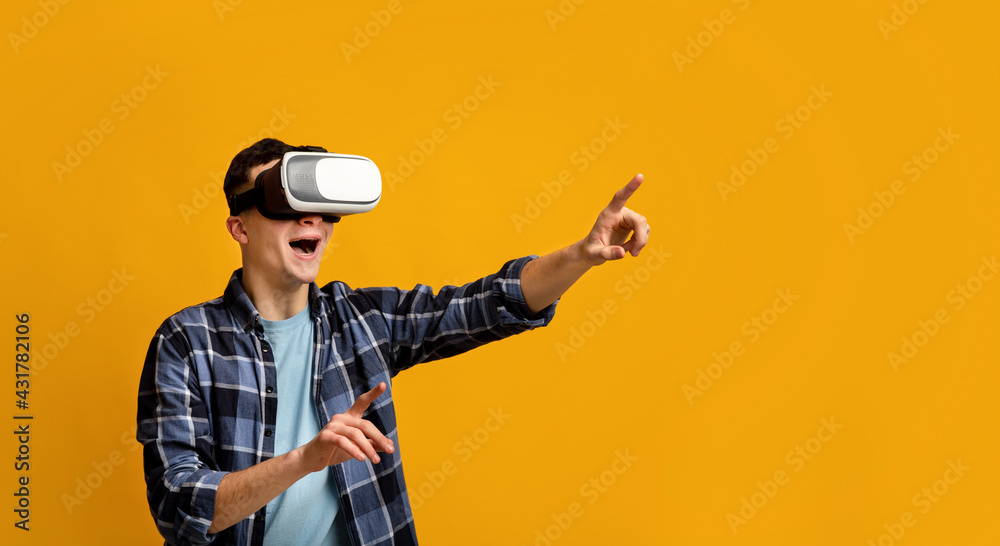 Cool young guy in virtual reality headset controlling cyber environment, pushing invisible button on virtual screen Cool young guy in virtual reality headset controlling cyber environment, pushing invisible button on virtual screen