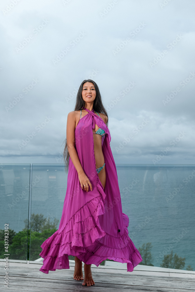 Stunning model in a purple cape poses while standing on the terrace against the backdrop of the seascape Stunning model in a purple cape poses while standing on the terrace against the backdrop of the seascape