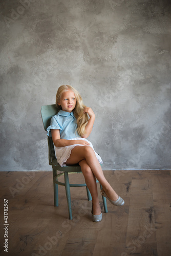 Girl is sitting on a chair and grimacing. Photo is great for demonstrating the character of a child - stubbornness, harmfulness, cunning, coquetry.
