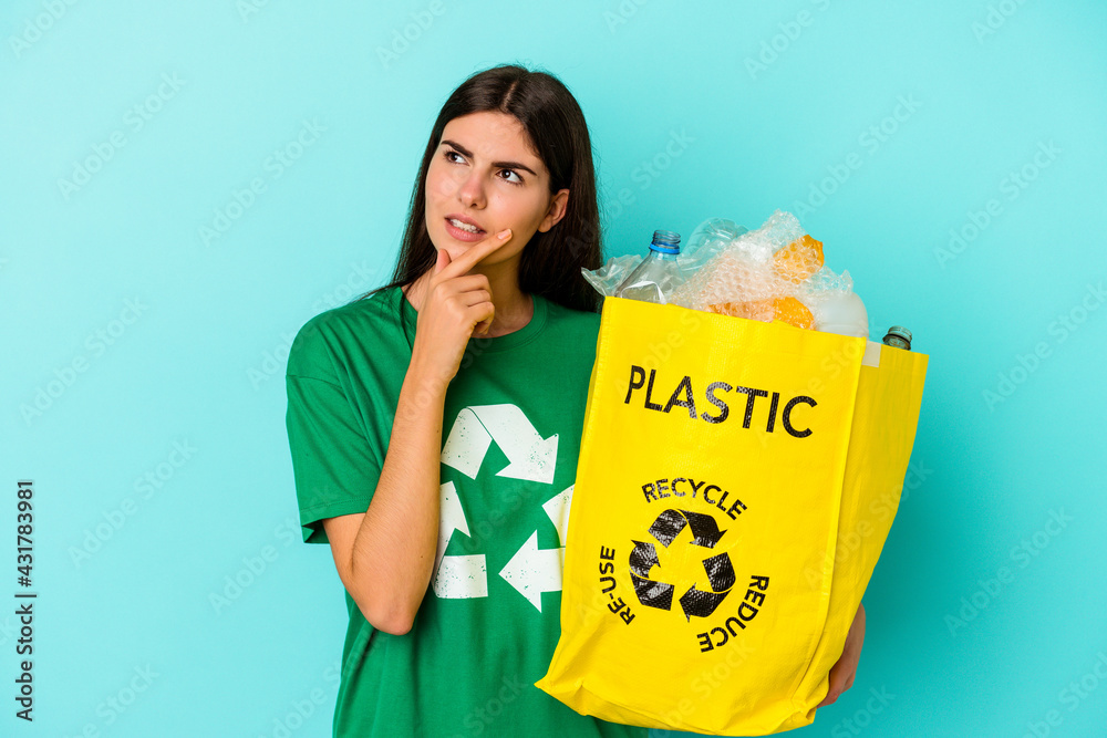 Young caucasian woman recycled plastic isolated on blue background looking sideways with doubtful and skeptical expression. Young caucasian woman recycled plastic isolated on blue background looking sideways with doubtful and skeptical expression.