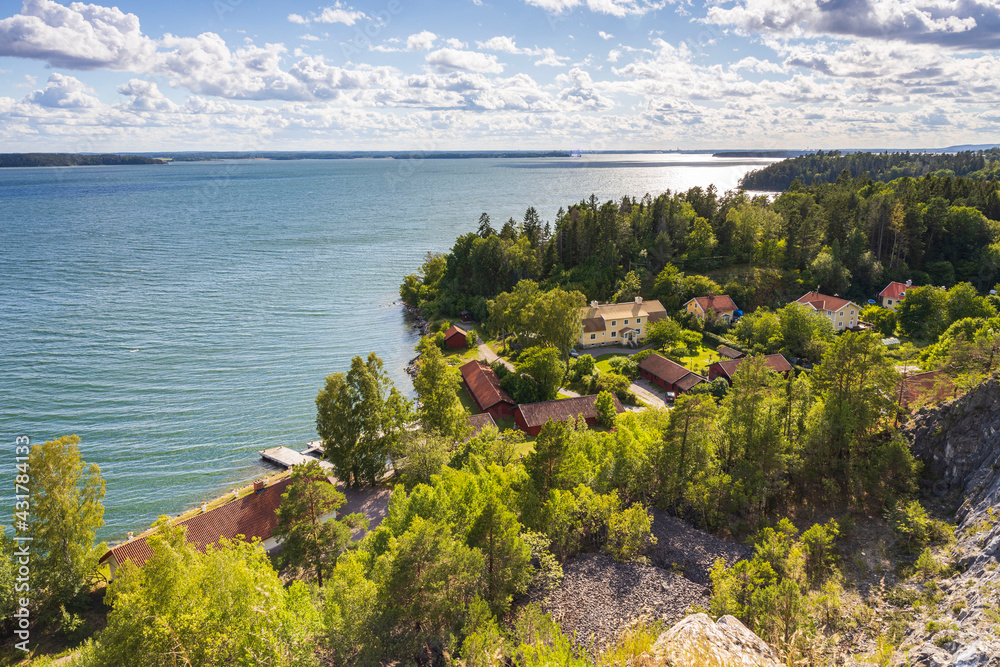 Beautiful nature coast landscape view. Buildings surrounded with green trees on lake surface and blue sky background. Sweden.