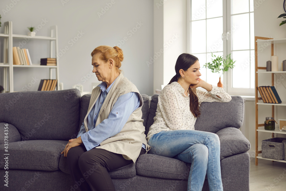 Family conflict. Offended older woman and her adult daughter or granddaughter are sitting on the couch with their backs to each other. Concept of misunderstanding between different generations. Family conflict. Offended older woman and her adult daughter or granddaughter are sitting on the couch with their backs to each other. Concept of misunderstanding between different generations.