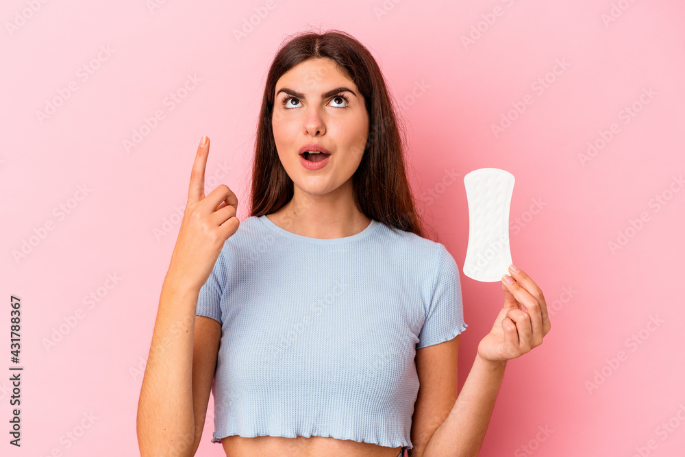 Young caucasian woman holding a compress isolated on pink background pointing upside with opened mouth. Young caucasian woman holding a compress isolated on pink background pointing upside with opened mouth.