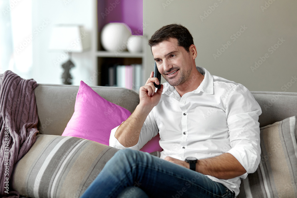 Close-up portrait of a handsome happy man making a phone call while sitting on a couch in his living room. Horizontal view. Close-up portrait of a handsome happy man making a phone call while sitting on a couch in his living room. Horizontal view.