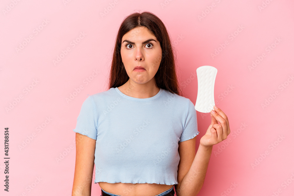 Young caucasian woman holding a compress isolated on pink background shrugs shoulders and open eyes confused. Young caucasian woman holding a compress isolated on pink background shrugs shoulders and open eyes confused.