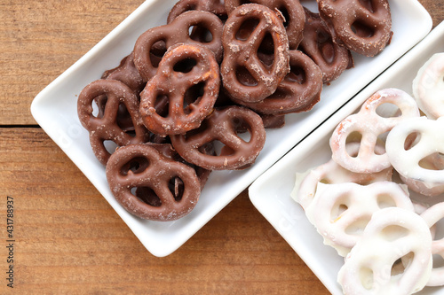 White and dark salted chocolate covered mini pretzels in a bowl on wood table. Homemade assorted mini pretzel chip cookies on plates on wooden background. Top view, copy space
