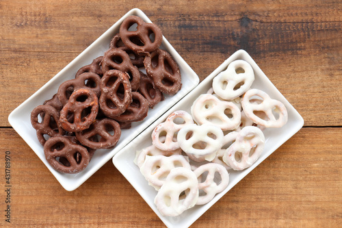 White and dark salted chocolate covered mini pretzels in a bowl on wood table. Homemade assorted mini pretzel chip cookies on plates on wooden background. Top view, copy space
 photo