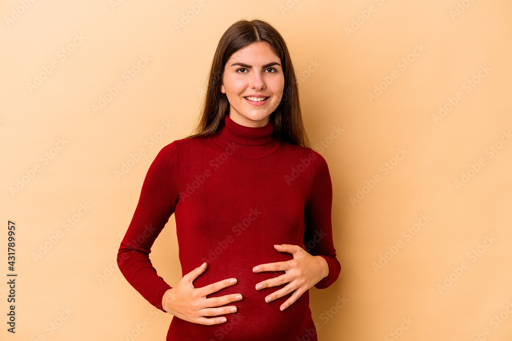 Obraz premium Young caucasian pregnant woman isolated on beige background happy, smiling and cheerful.